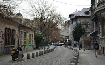 Cobblestone street in Bucharest with historic buildings and a dome in the background.