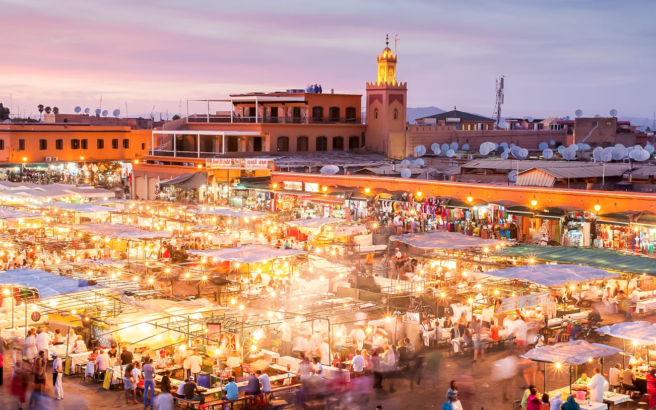 Marrakech night market bustling with people and food stalls under vibrant lights.