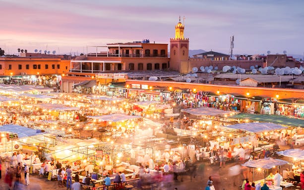 Marrakech night market bustling with people and food stalls under vibrant lights.