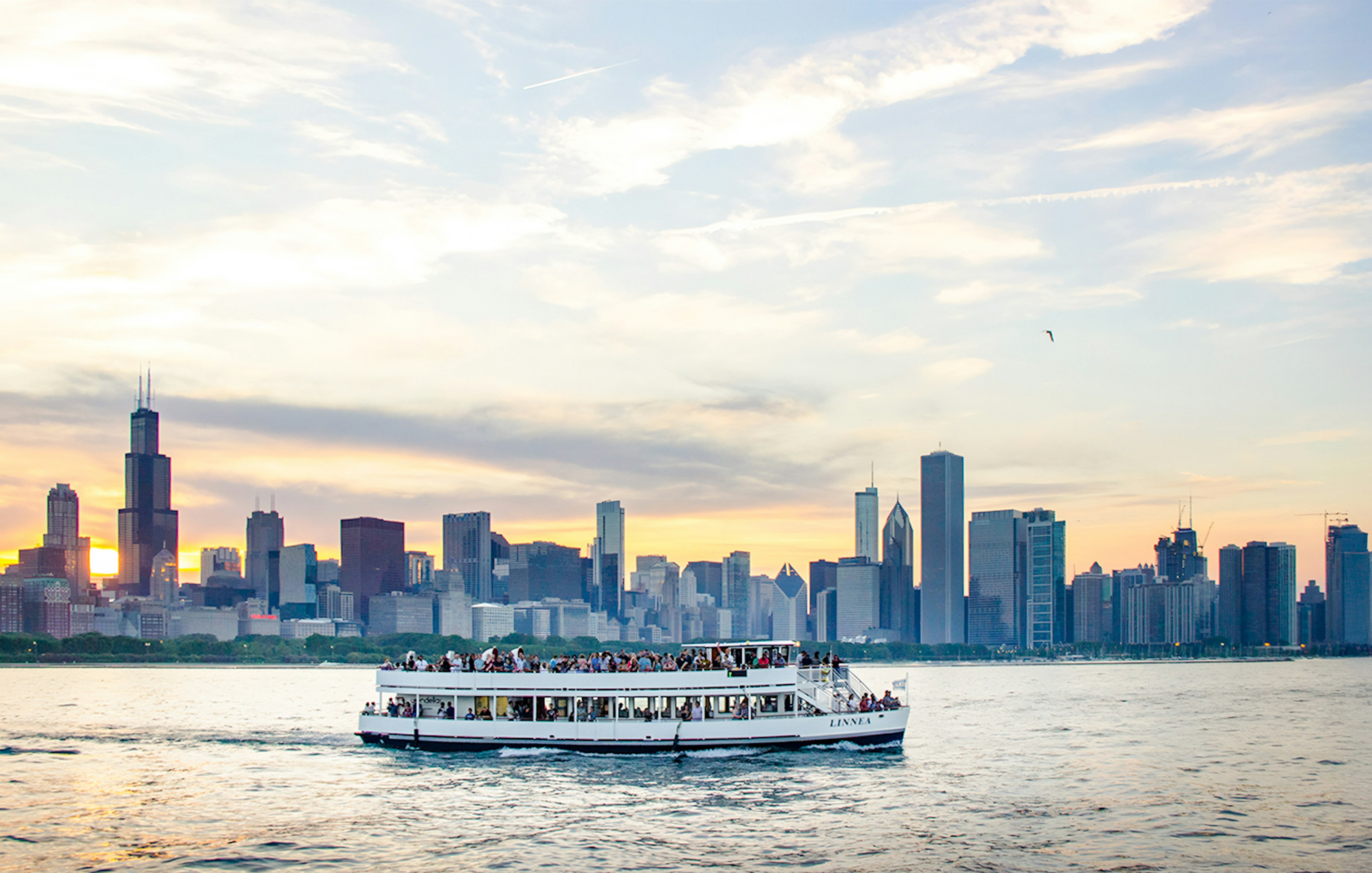 Cruise boat on Lake Michigan with Chicago skyline at sunset.