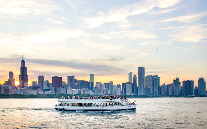 Cruise boat on Lake Michigan with Chicago skyline at sunset.