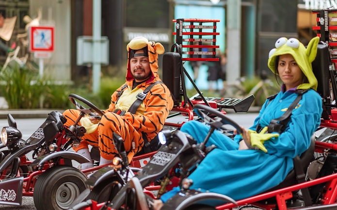 Couple in costumes driving go-karts on Asakusa tour, Tokyo.