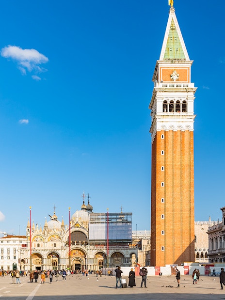 St. Mark's Basilica and Campanile in Venice, Italy, with tourists in the square.