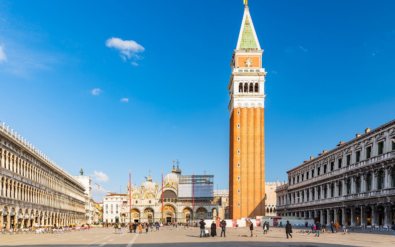 St. Mark's Basilica and Campanile in Venice, Italy, with tourists in the square.
