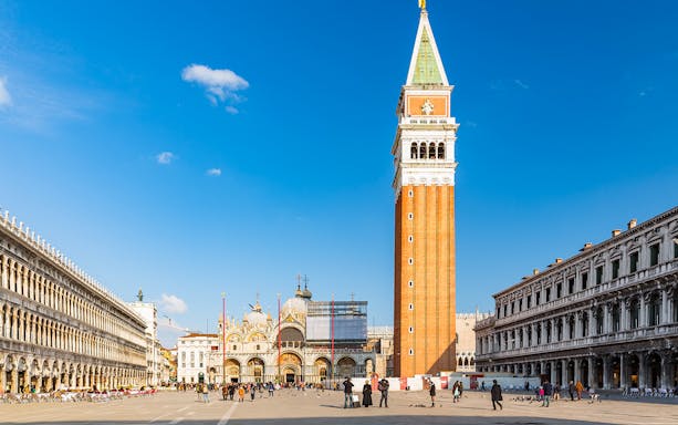 St. Mark's Basilica and Campanile in Venice, Italy, with tourists in the square.