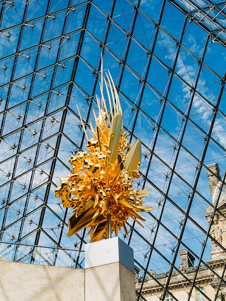 Louvre Museum glass pyramid interior with golden sculpture.
