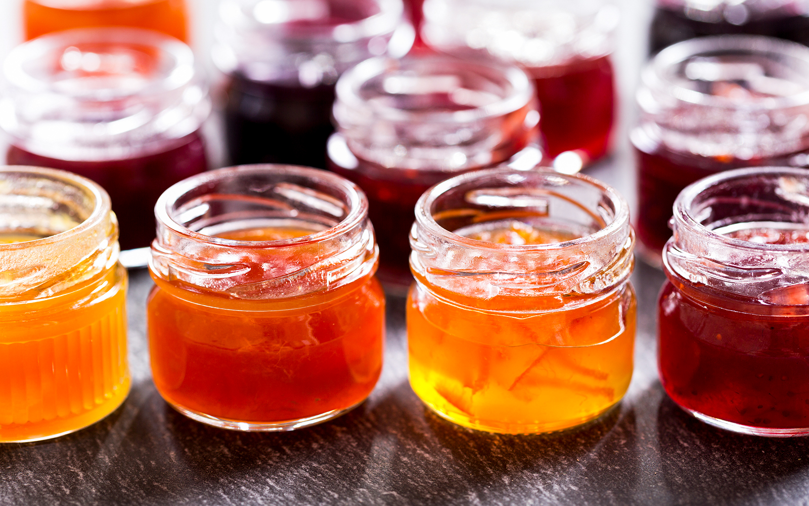 Jars of assorted fruit jam on a dark surface.