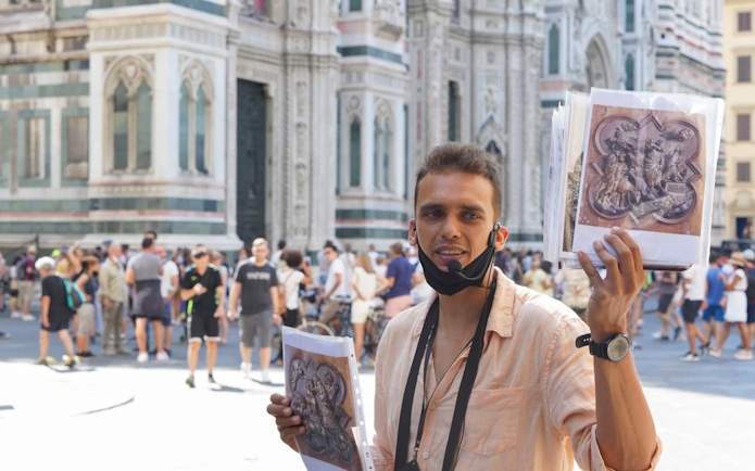 Tour guide in front of Florence Cathedral holding art prints during walking tour.
