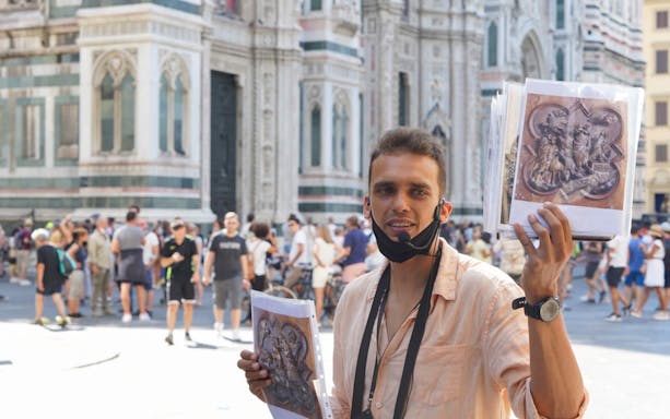 Tour guide in front of Florence Cathedral holding art prints during walking tour.