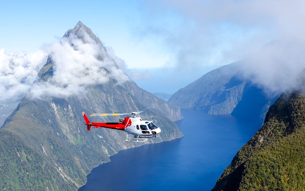Helicopter flying over cloud-covered fiords in Milford Sound, New Zealand.