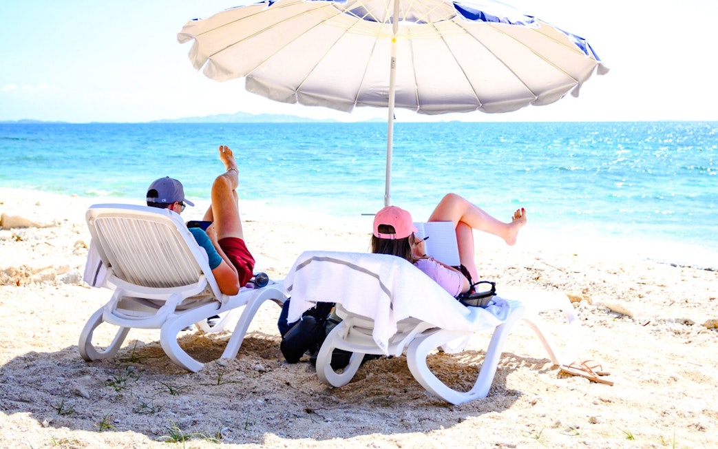 Couple relaxing on lounge chairs under an umbrella at South Sea Island, Fiji beach.