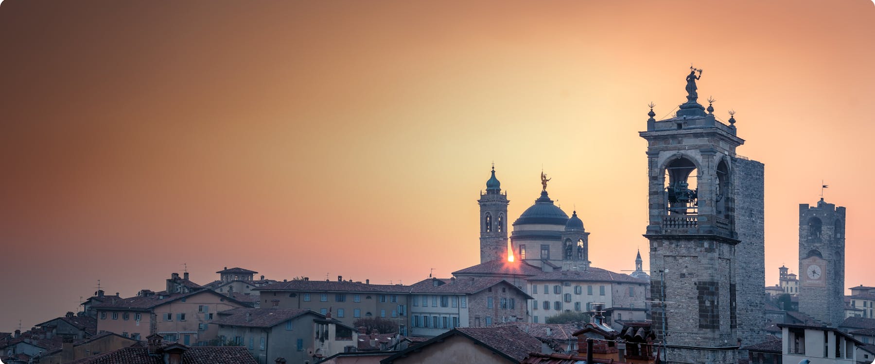 Bergamo skyline at sunset with historic towers and domes.