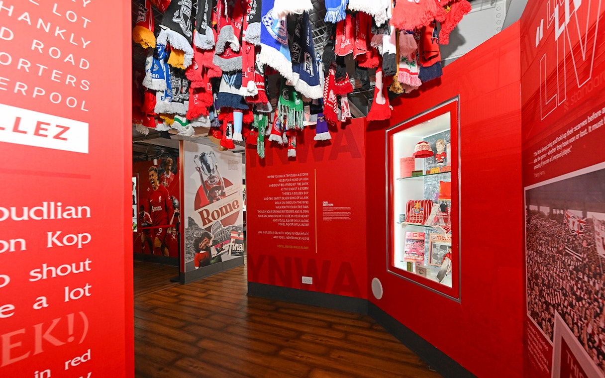 Liverpool FC stadium tour exhibit with scarves and memorabilia display.