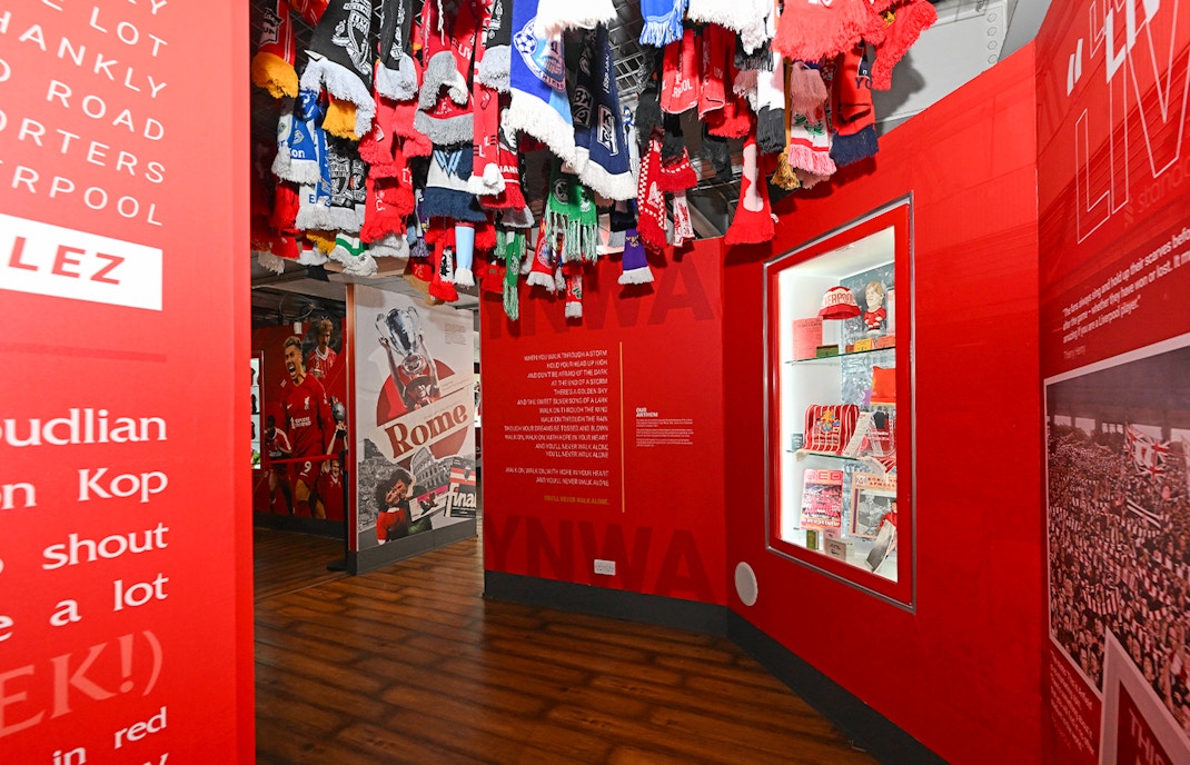 Liverpool FC stadium tour exhibit with scarves and memorabilia display.
