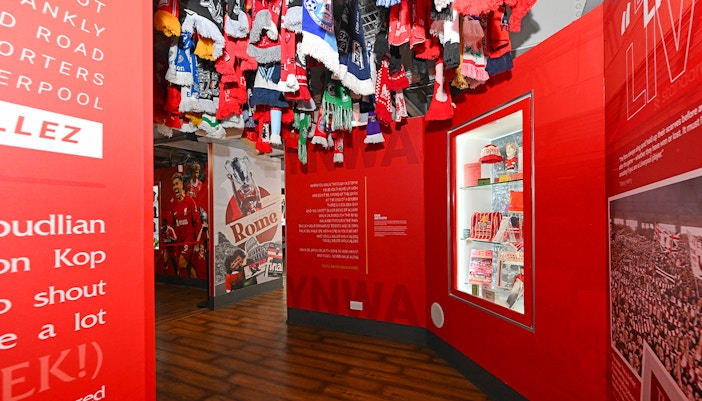 Liverpool FC stadium tour exhibit with scarves and memorabilia display.