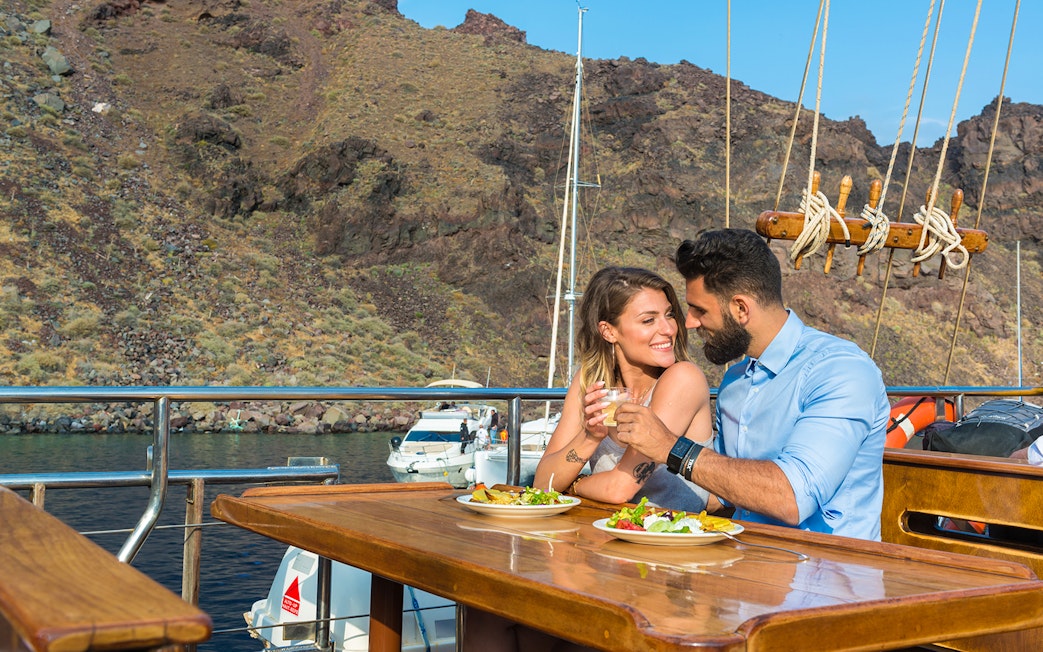 Couple dining on a boat near volcanic islands with scenic views.