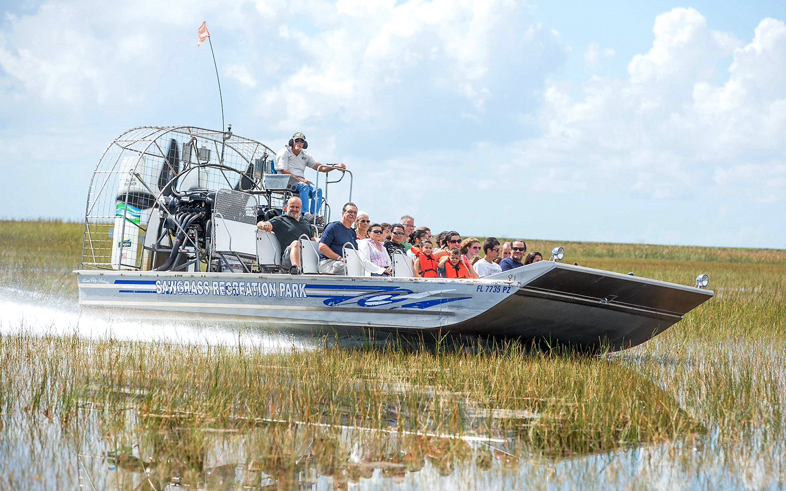 Airboat with tourists gliding through Everglades marshland at Sawgrass Recreation Park.