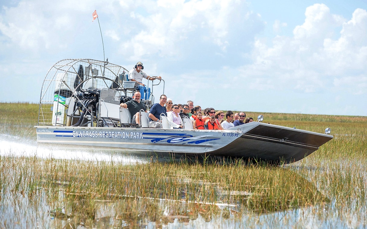 Airboat with tourists gliding through Everglades marshland at Sawgrass Recreation Park.