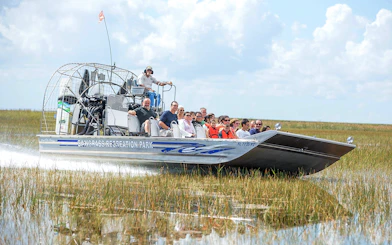 Airboat with tourists gliding through Everglades marshland at Sawgrass Recreation Park.