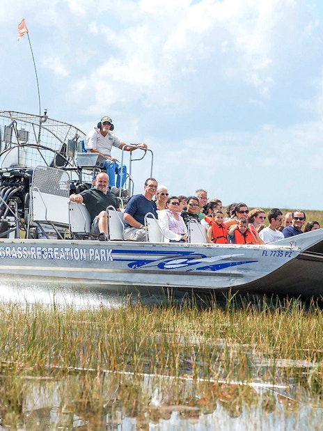 Airboat with tourists gliding through Everglades marshland at Sawgrass Recreation Park.