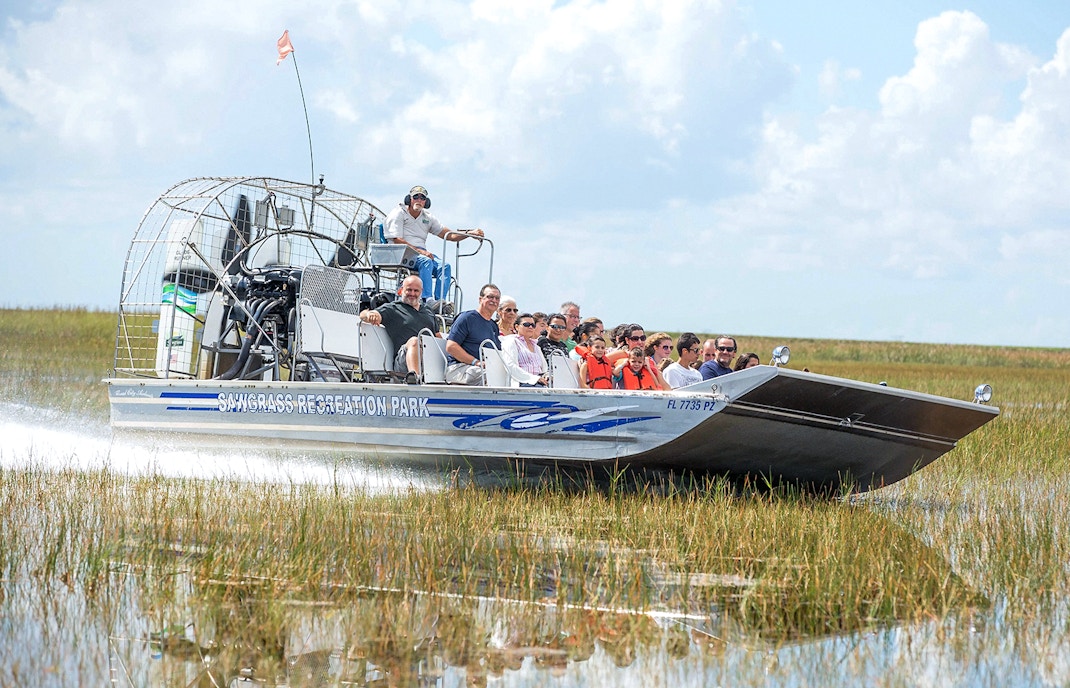 Airboat with tourists gliding through Everglades marshland at Sawgrass Recreation Park.