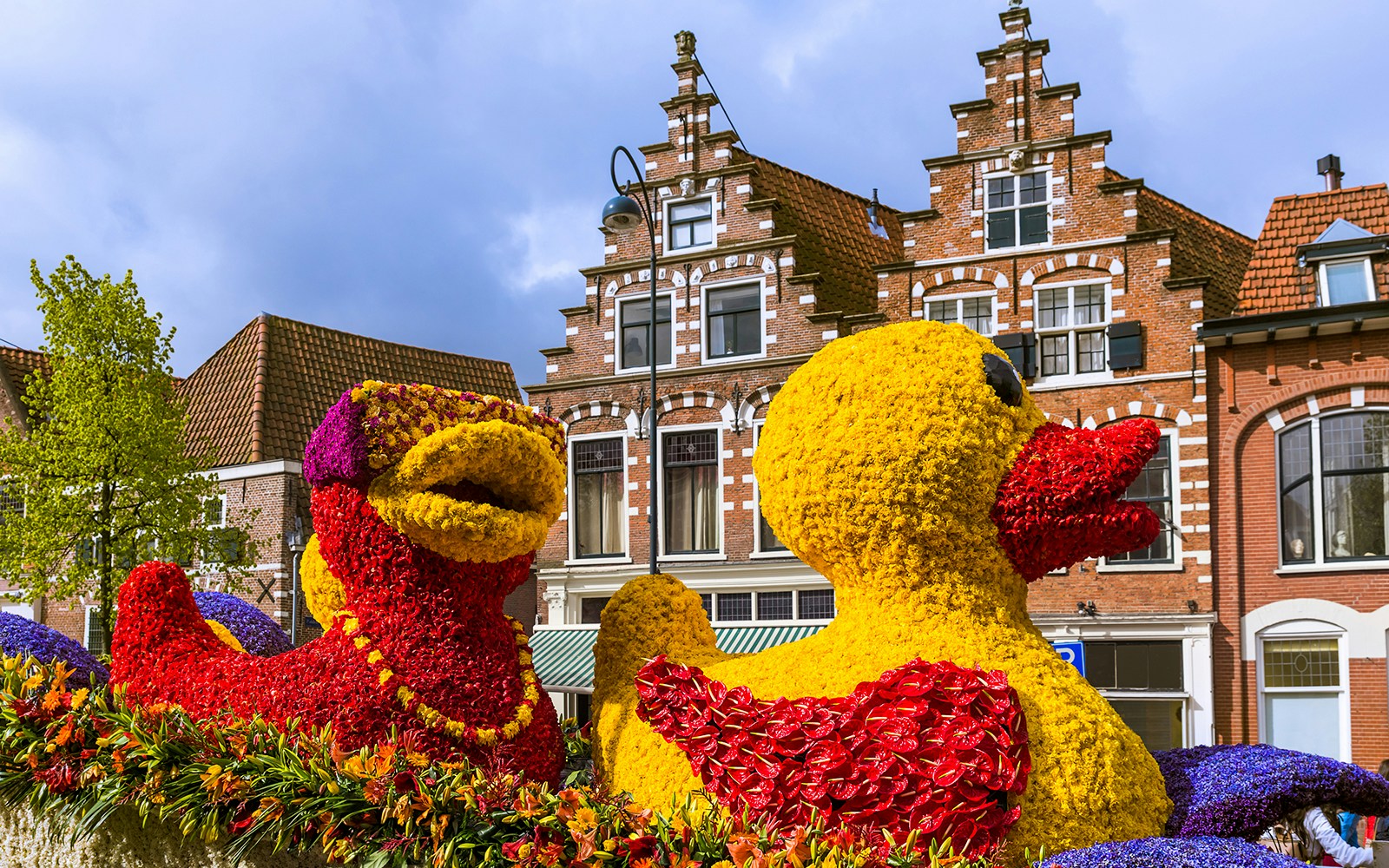 Versierde bloemenwagens trekken langs huizen met klassieke Nederlandse architectuur