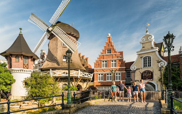 Family walking near windmill and historic buildings at Heide Park, Germany.