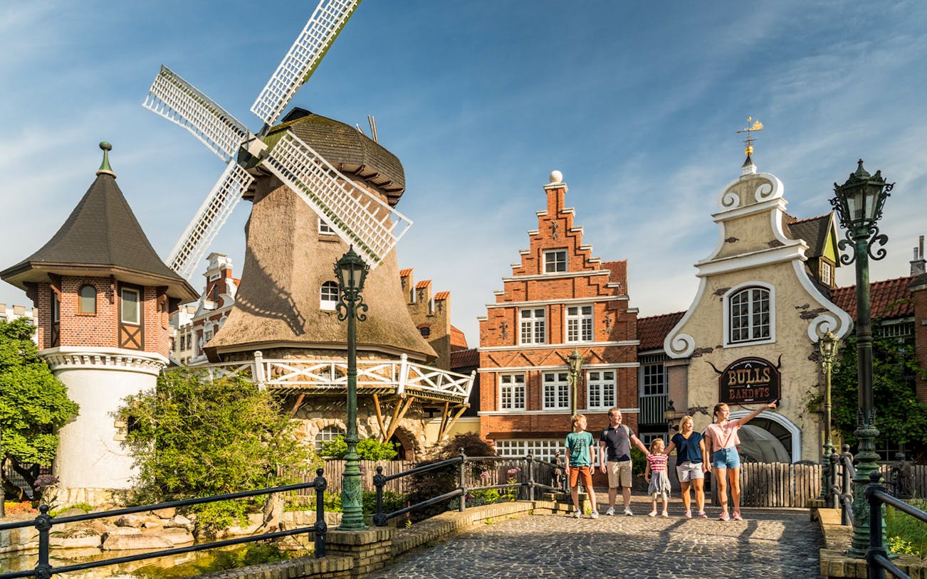 Family walking near windmill and historic buildings at Heide Park, Germany.