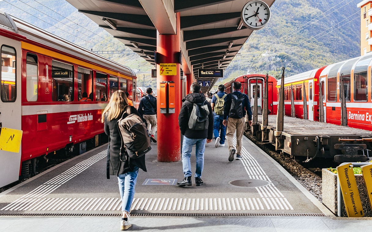 Travelers boarding the Bernina Red Train at a station in St. Moritz, surrounded by mountains.