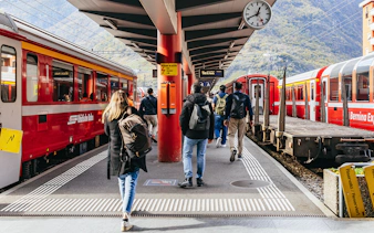 Travelers boarding the Bernina Red Train at a station in St. Moritz, surrounded by mountains.