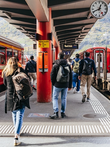 Travelers boarding the Bernina Red Train at a station in St. Moritz, surrounded by mountains.