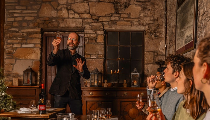 Guide leading guests in Edinburgh Whiskey Tasting Tour, showcasing whiskey samples and historic underground setting.