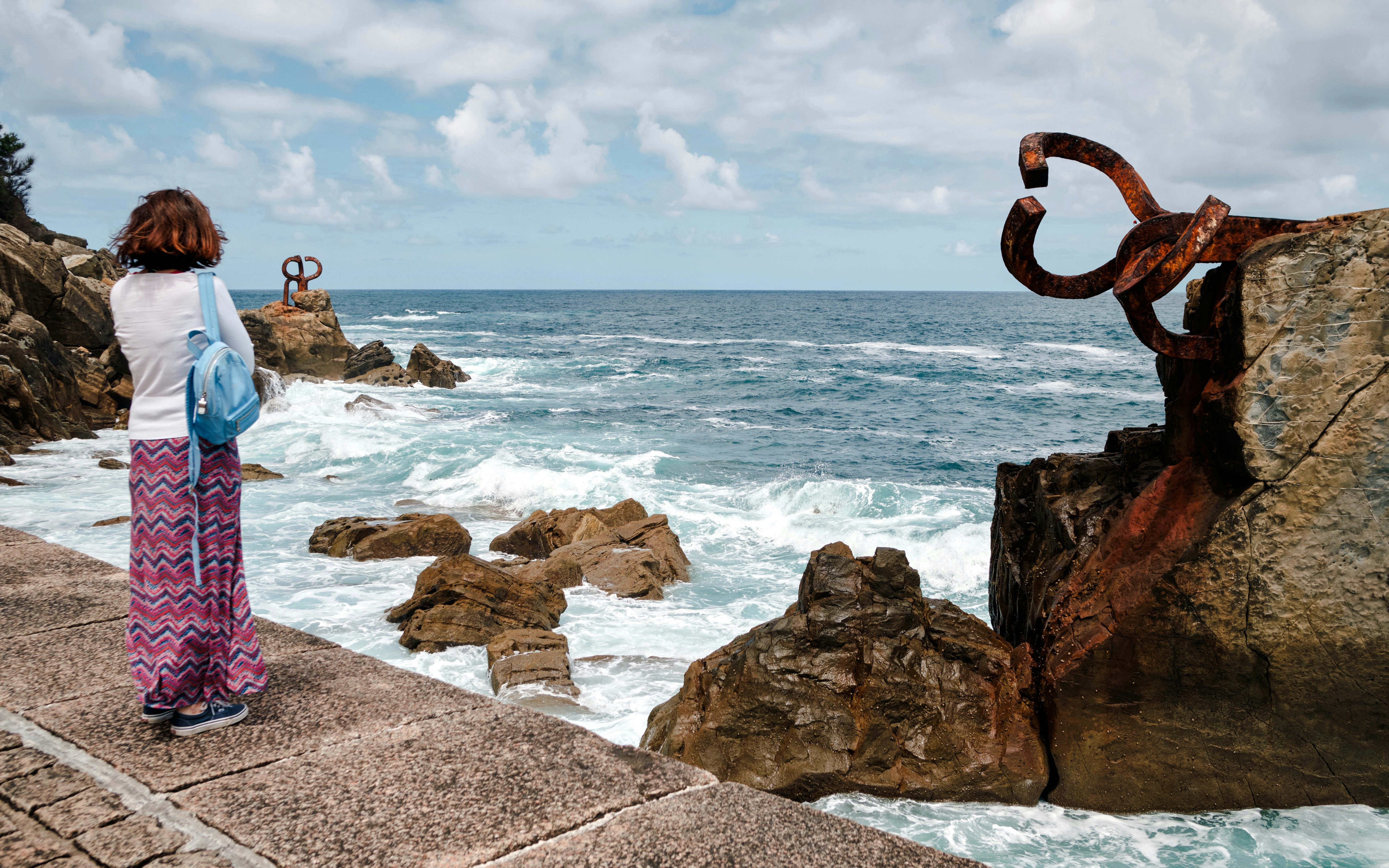 Frau betrachtet die Skulpturen „Peine del Viento“ an der felsigen Küste in San Sebastián, Baskenland, Spanien.