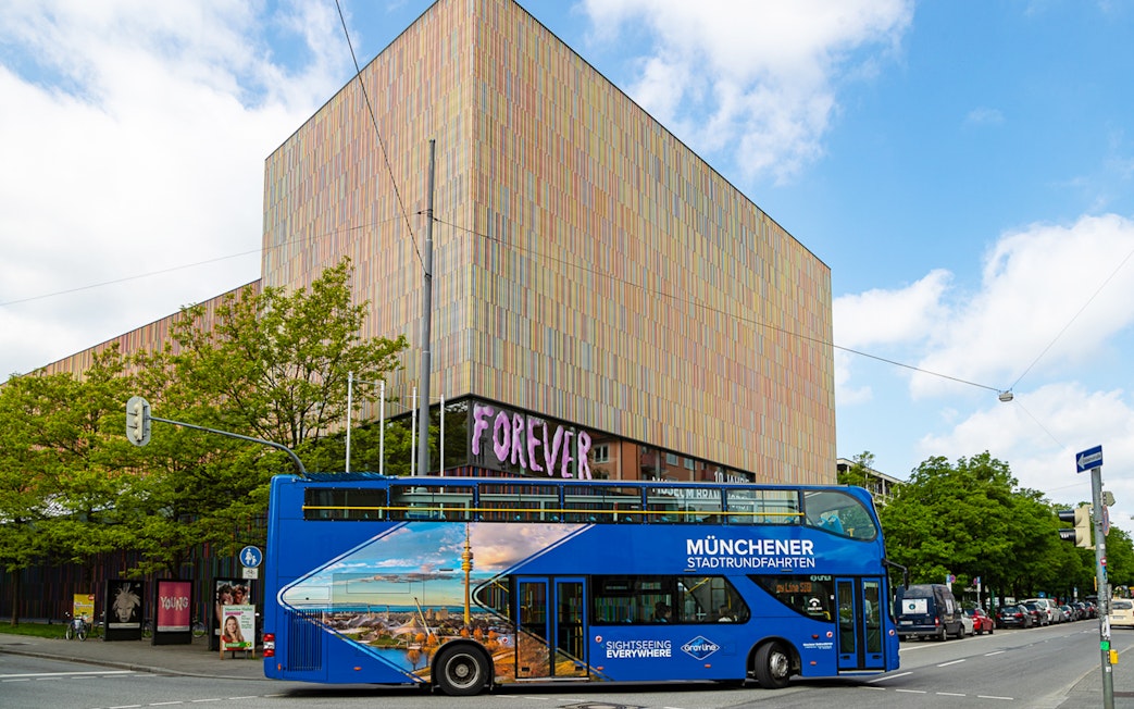 Blue double-decker tour bus in Munich near a modern art museum, part of city and FC Bayern Munich arena tour.