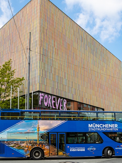 Blue double-decker tour bus in Munich near a modern art museum, part of city and FC Bayern Munich arena tour.