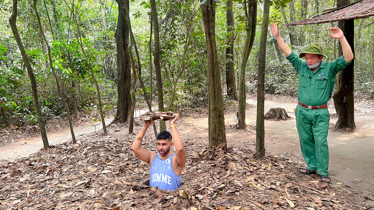 Man standing in Cu Chi Tunnel holding cover, Ho Chi Minh City, Vietnam.