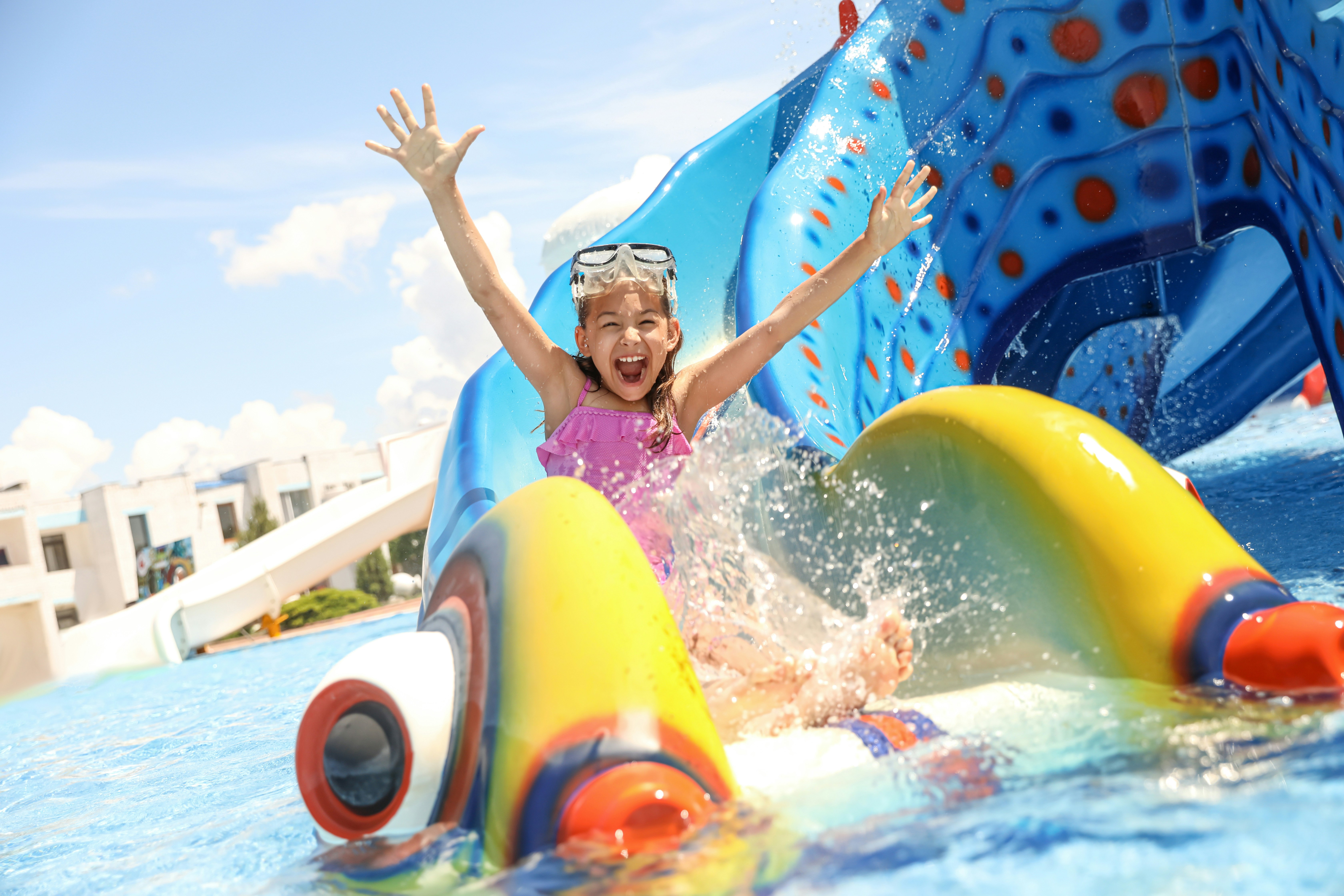 Little girl sliding down colorful water slide at a water park.
