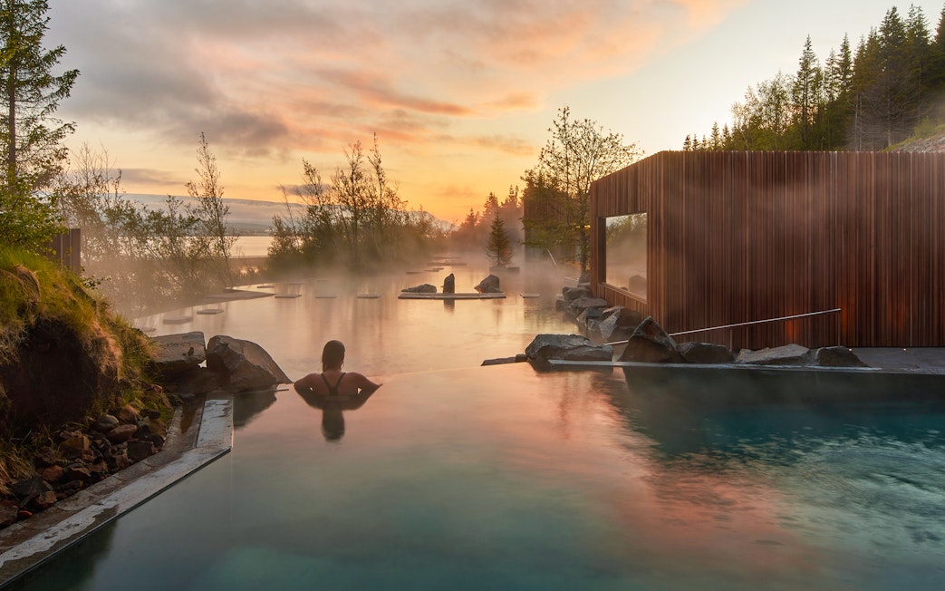 Person relaxing in Forest Lagoon geothermal spa at sunset, Vaðlaskógur forest, Akureyri, North Iceland.