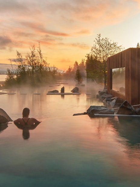 Person relaxing in Forest Lagoon geothermal spa at sunset, Vaðlaskógur forest, Akureyri, North Iceland.