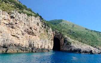 Haxhi Ali Cave entrance along rocky coastline with clear blue water in Albania.