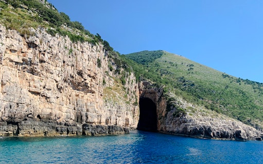 Haxhi Ali Cave entrance along rocky coastline with clear blue water in Albania.