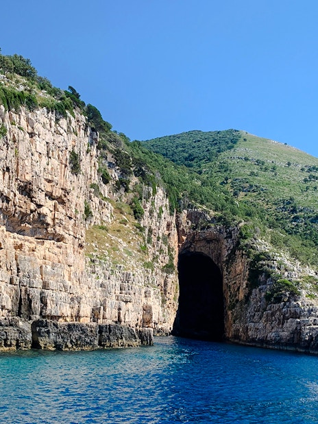 Haxhi Ali Cave entrance along rocky coastline with clear blue water in Albania.