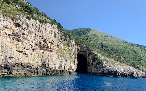 Haxhi Ali Cave entrance along rocky coastline with clear blue water in Albania.