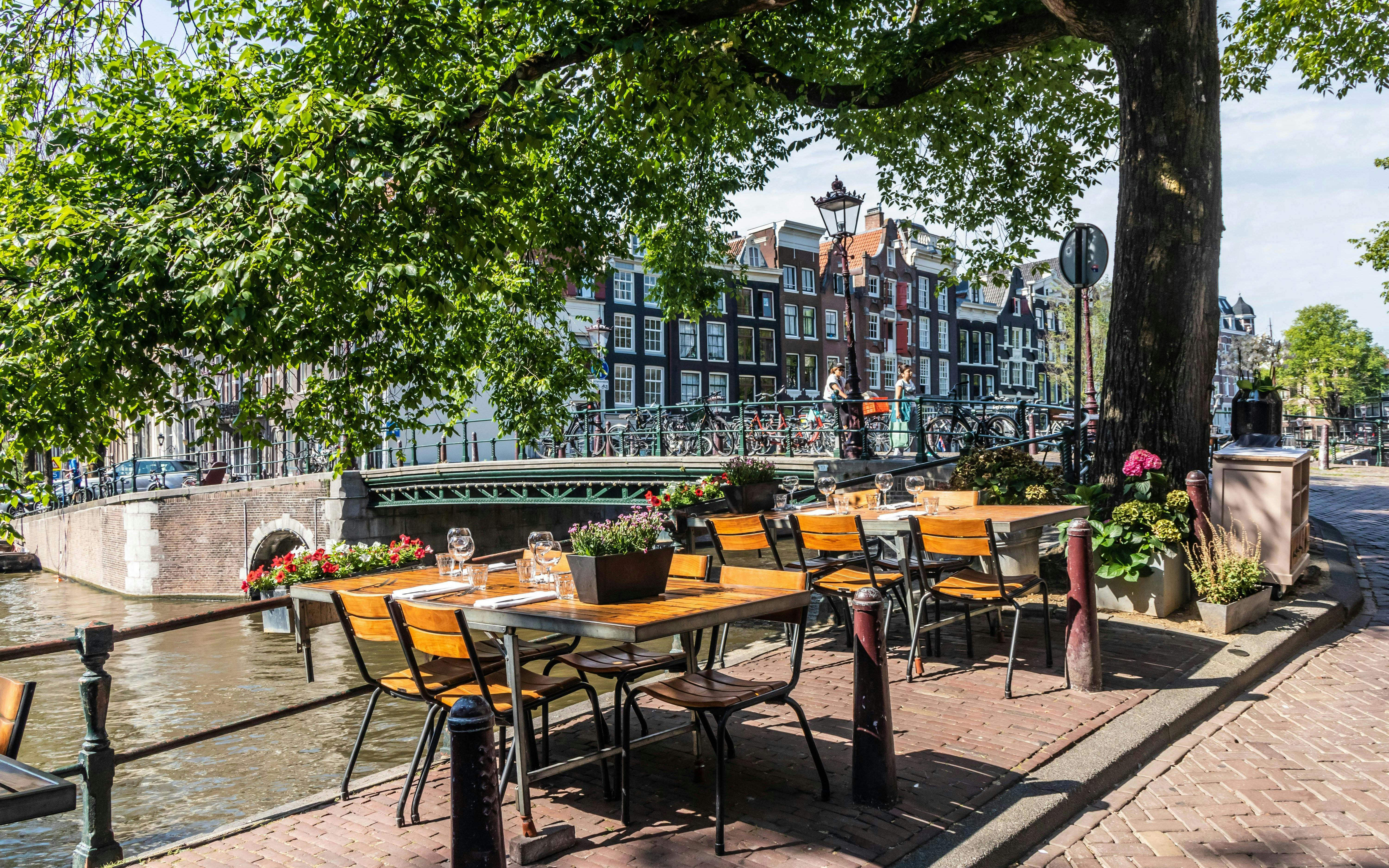 Outdoor cafe seating along Brouwersgracht canal in Amsterdam with historic buildings in view.