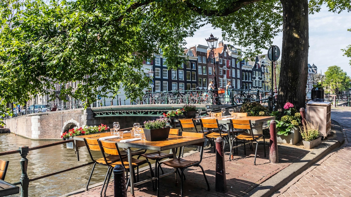 Outdoor cafe seating along Brouwersgracht canal in Amsterdam with historic buildings in view.