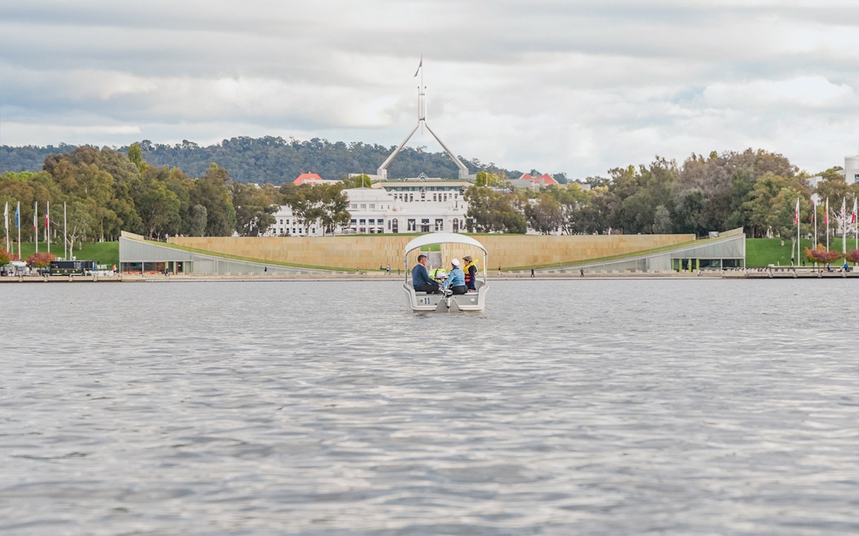 Electric picnic boat on Lake Burley Griffin with Canberra's Parliament House in view.