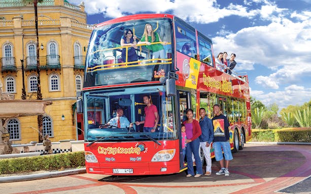 Hop-on hop-off bus with people boarding near a historic building in Johannesburg.