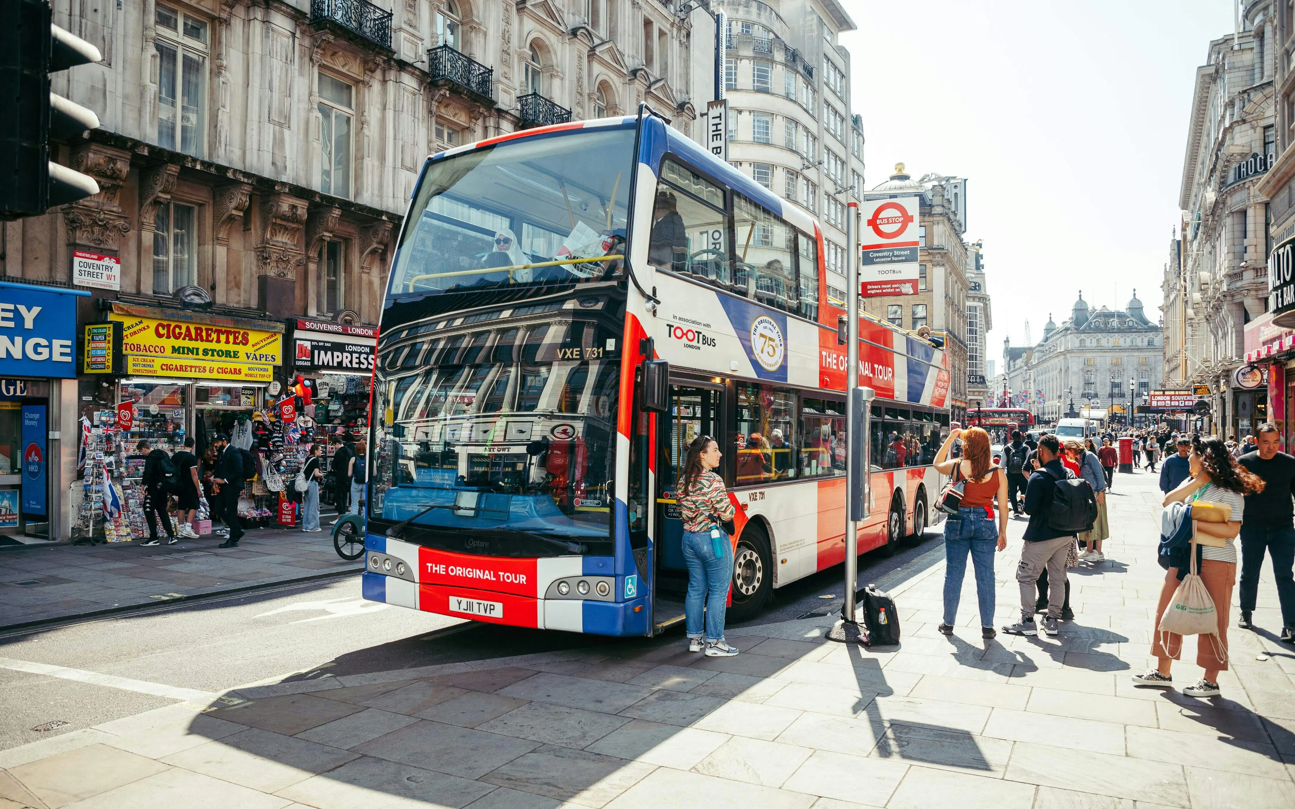 Hop-on hop-off bus at a busy London street near Coventry Street.