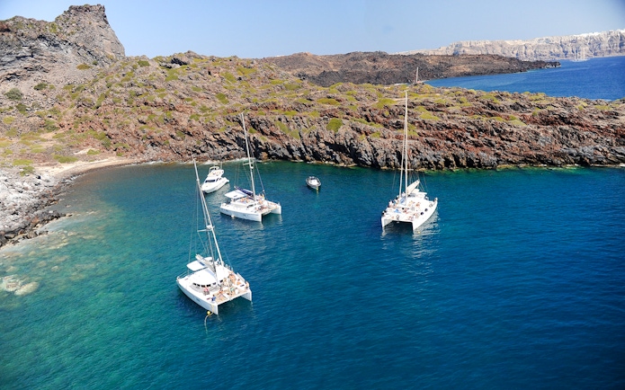 Catamarans anchored in a secluded bay during a Santorini luxury cruise.