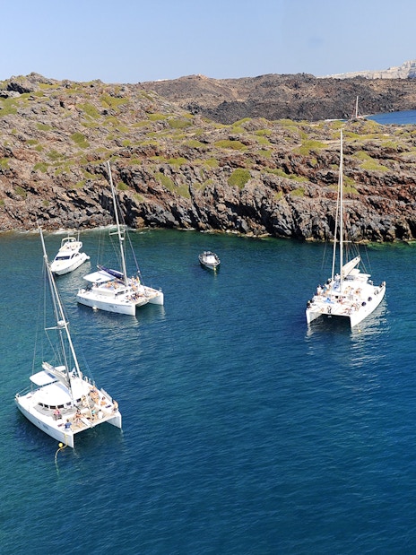 Catamarans anchored in a secluded bay during a Santorini luxury cruise.